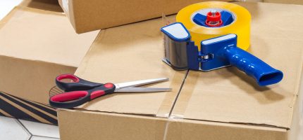 Packing tape dispenser, scissors on the cardboard box.